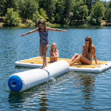 Three people enjoy a sunny day on a lake with inflatable floating platforms. 