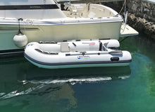 Island Hopper White Marlin 9.8′ Inflatable Fishing Boat floating in  water next to a white motorboat docked at a harbor.