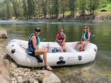 Three people in an inflatable raft on a river with trees and rocks in the background
